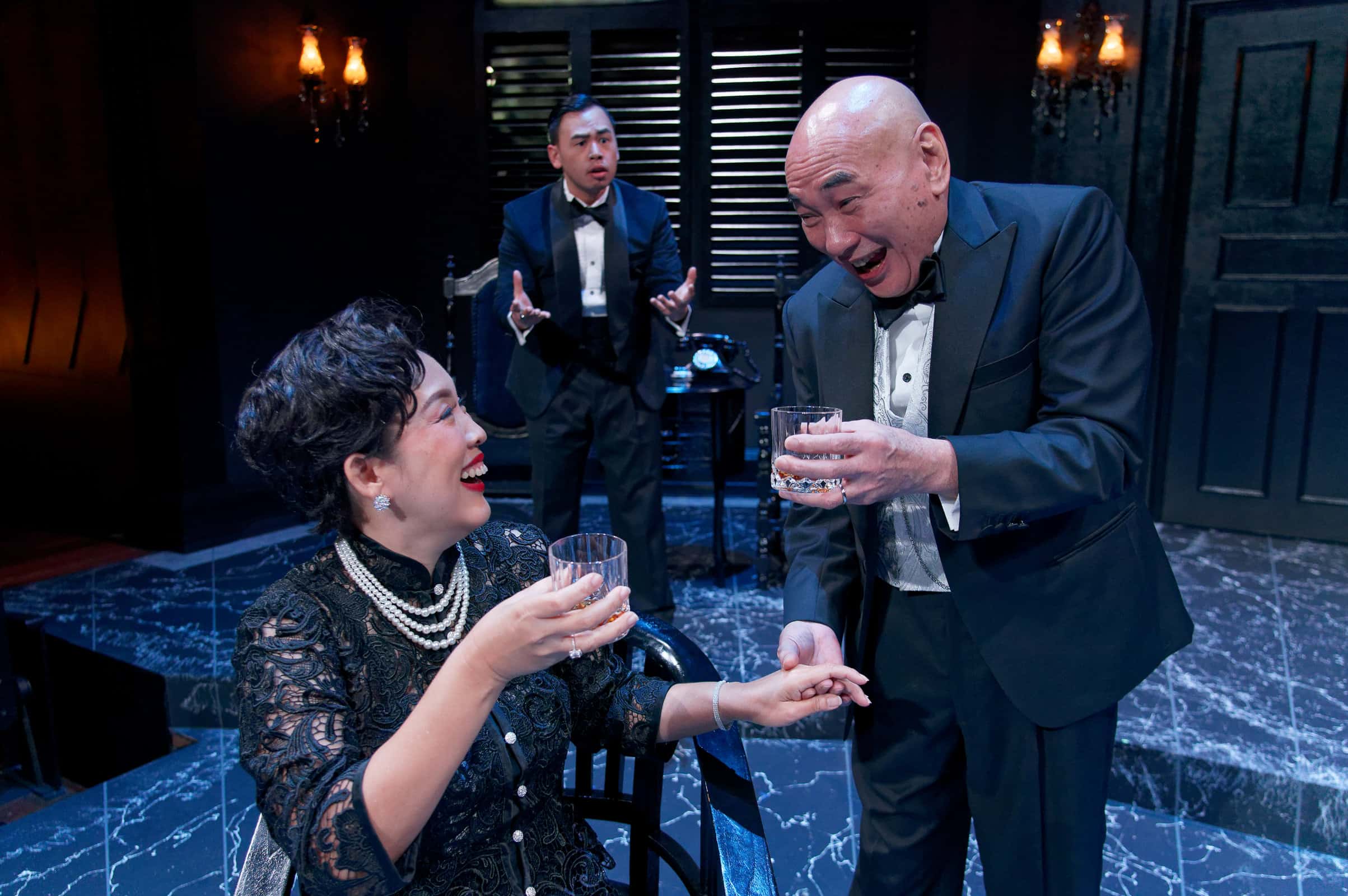 Serene Chen as Sybil Ling and Lim Kay Siu as Arthur Ling having a cheerful conversation over a drink as Dennis Sofian as Eric Ling look at them with a troubled look in the background