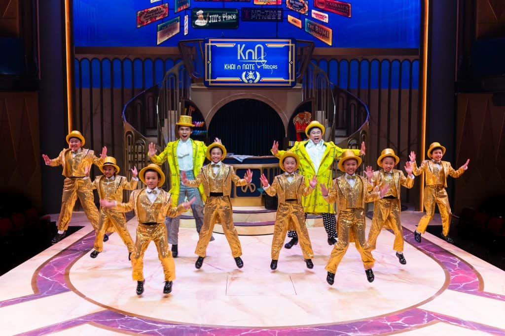 Rino Junior John as Nate, Izzul Irfan as Khai and the First Stage Kids dressed in gold and yellow, tap dancing on stage